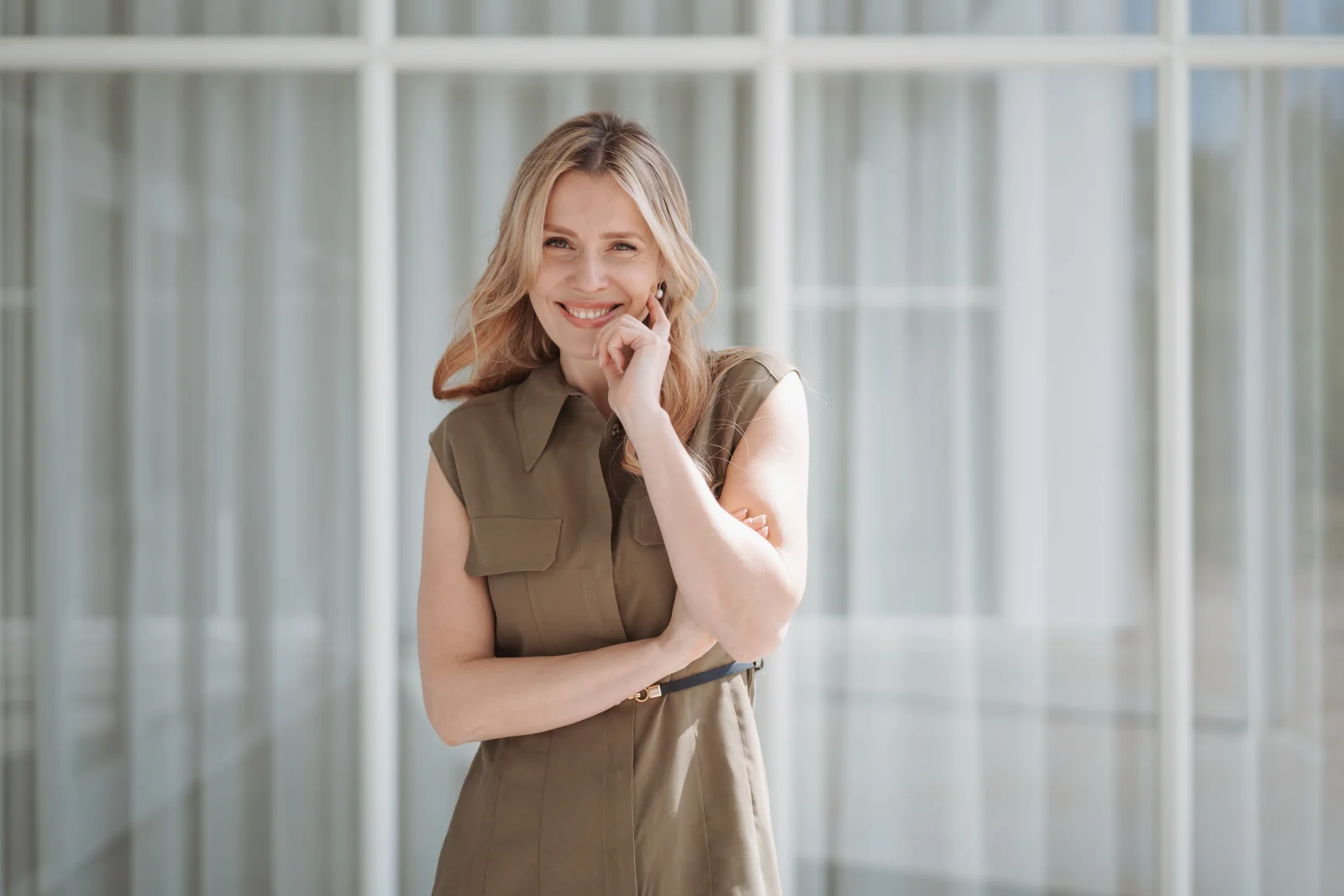 Lana Kern lächelnd im olivgrünen Kleid vor einer Fensterfront